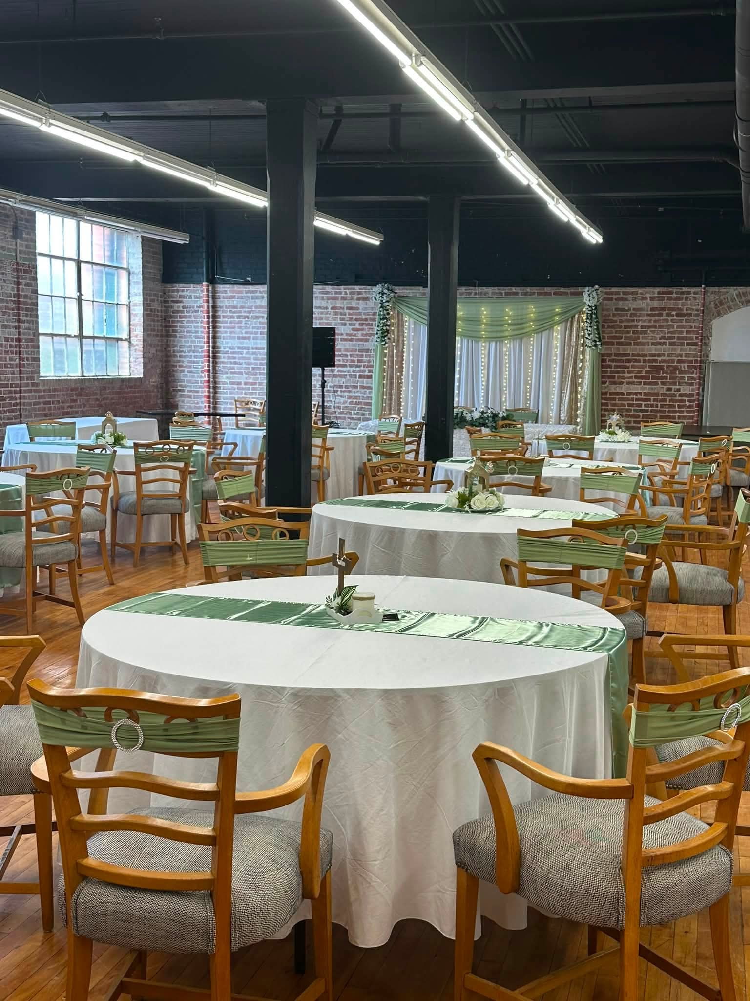 Wedding reception hall in Cambridge MD set with round tables, white linens and sage green runners under exposed brick