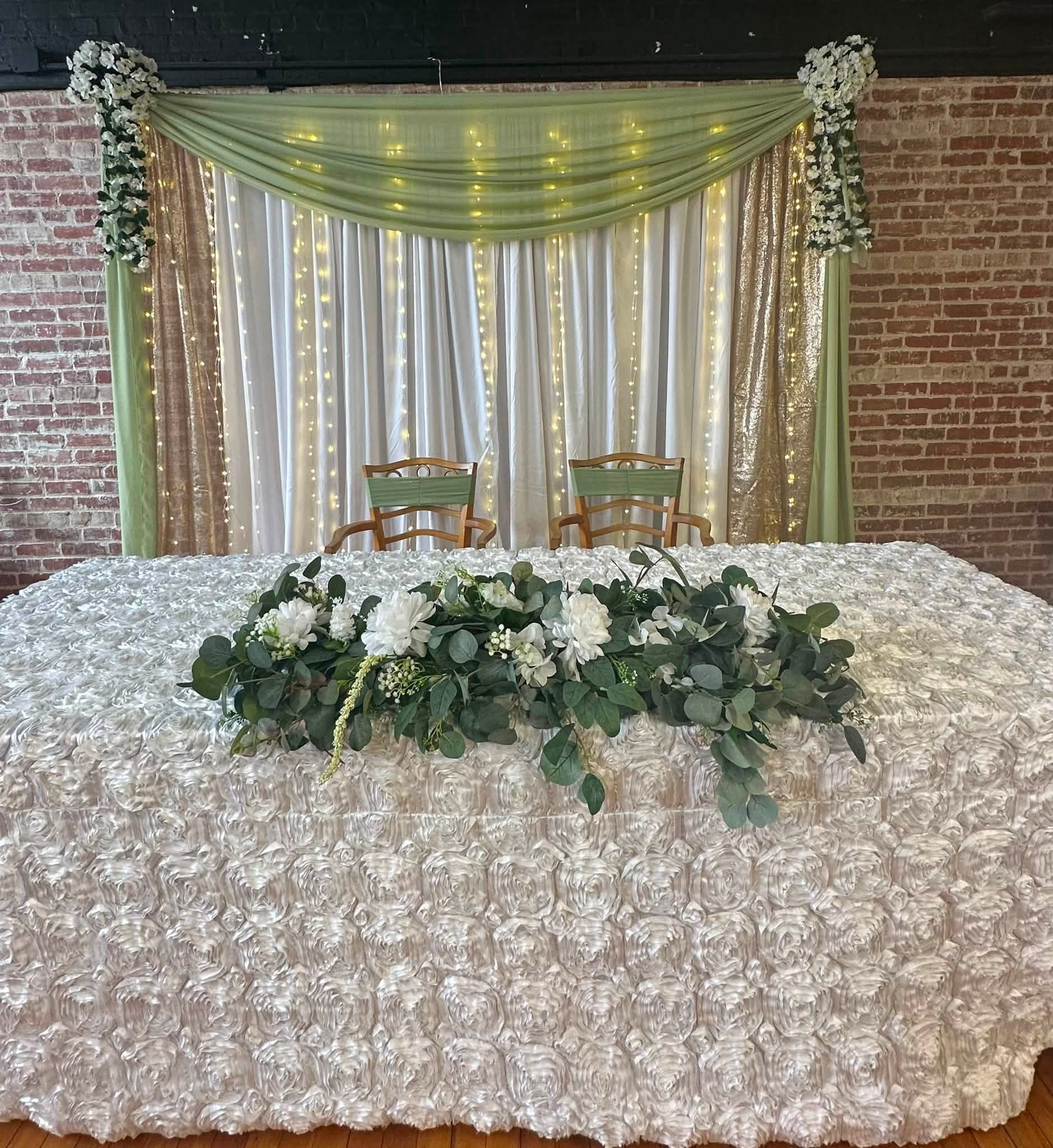 Wedding ceremony backdrop and sweetheart table with draped fabric and string lights at a Cambridge MD wedding venue